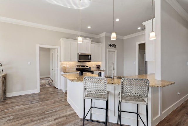 kitchen with appliances with stainless steel finishes, hanging light fixtures, a peninsula, white cabinetry, and a sink