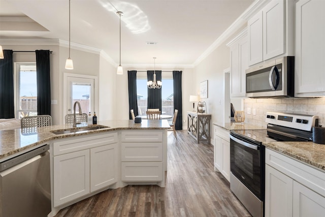 kitchen with hanging light fixtures, a sink, stainless steel appliances, white cabinetry, and backsplash