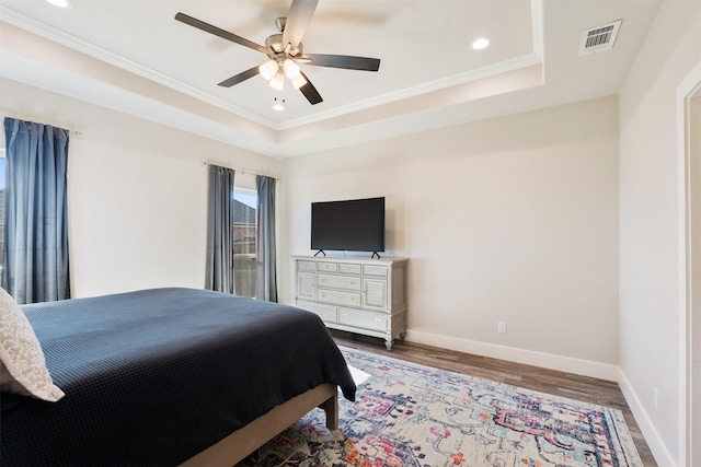 bedroom with baseboards, visible vents, a raised ceiling, ornamental molding, and wood finished floors