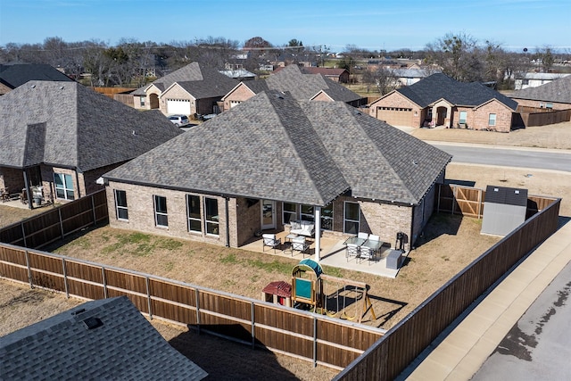 rear view of house with a shingled roof, a residential view, a playground, and a fenced backyard