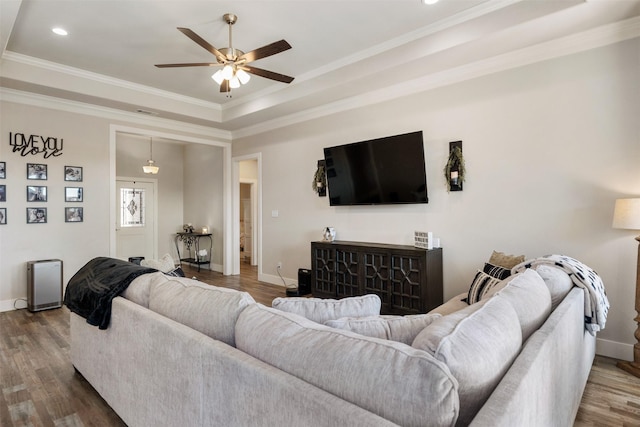 living area with wood finished floors, a raised ceiling, and crown molding