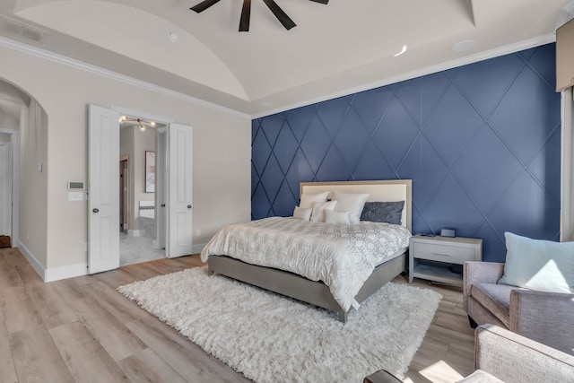 bedroom featuring arched walkways, crown molding, light wood finished floors, an accent wall, and baseboards