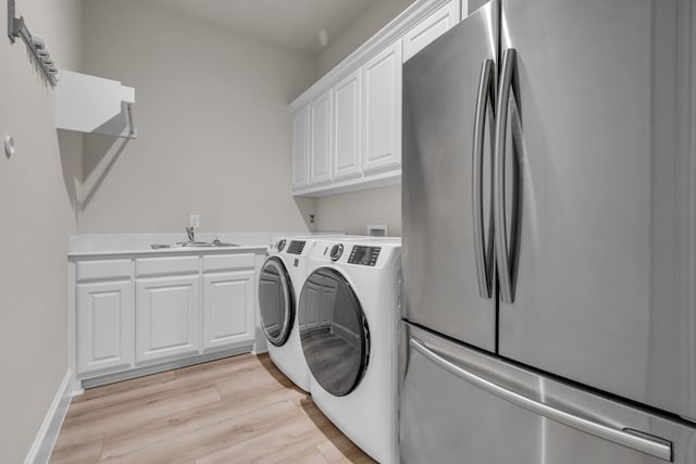 laundry area featuring cabinet space, baseboards, washer and clothes dryer, light wood-style flooring, and a sink