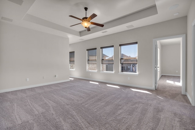 carpeted empty room featuring ceiling fan, a raised ceiling, visible vents, and baseboards