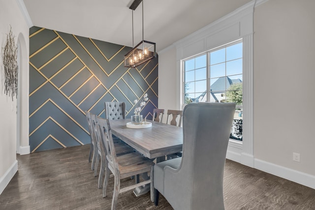 dining space featuring baseboards, an accent wall, ornamental molding, wood finished floors, and a notable chandelier