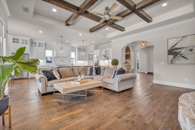 living area featuring arched walkways, dark wood-type flooring, ceiling fan, coffered ceiling, and baseboards