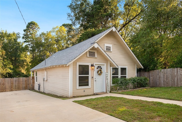 view of front facade featuring a patio, an outbuilding, roof with shingles, fence, and a front lawn