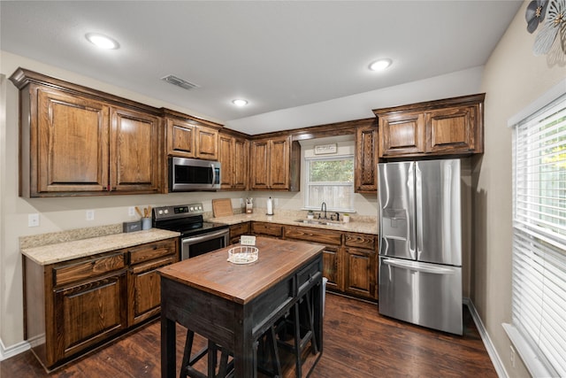 kitchen with dark wood finished floors, visible vents, appliances with stainless steel finishes, a sink, and a kitchen island