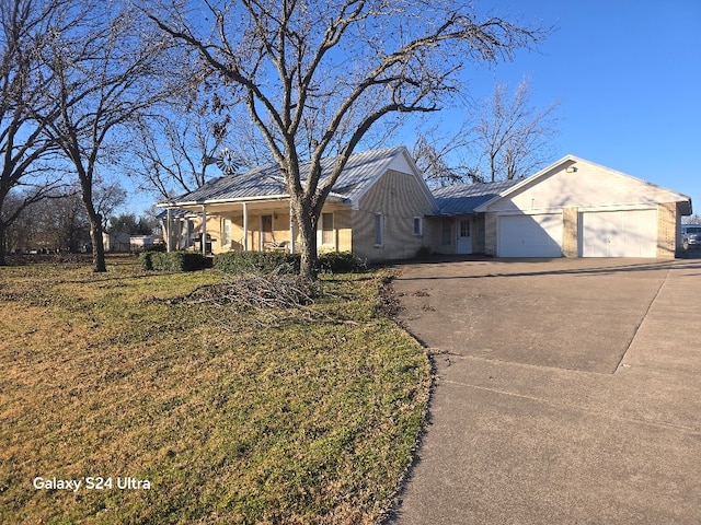 ranch-style house featuring metal roof, covered porch, a garage, driveway, and a front lawn