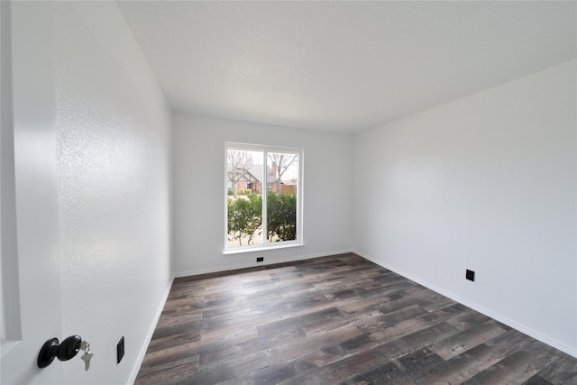 spare room featuring baseboards and dark wood finished floors