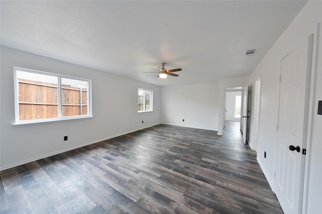 empty room with dark wood-style floors, baseboards, visible vents, and a ceiling fan