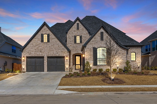 french provincial home featuring driveway, a shingled roof, a garage, and brick siding