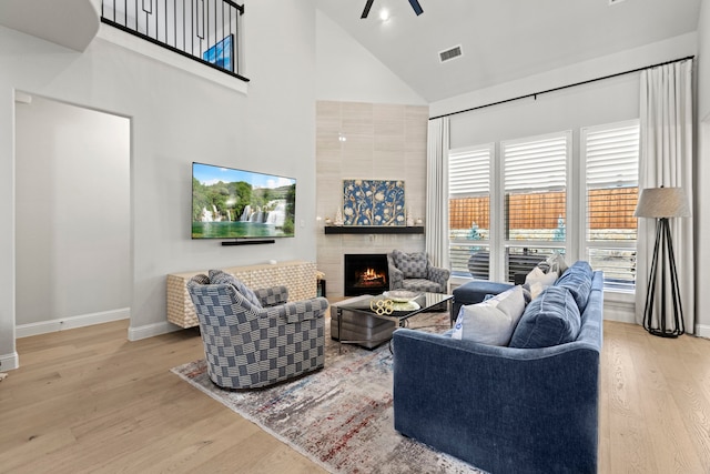 living room with a fireplace, visible vents, a high ceiling, wood finished floors, and baseboards