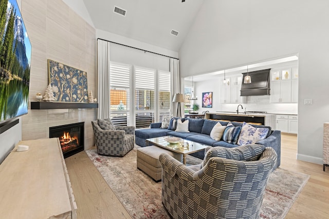 living area featuring high vaulted ceiling, a tile fireplace, visible vents, and light wood-style floors