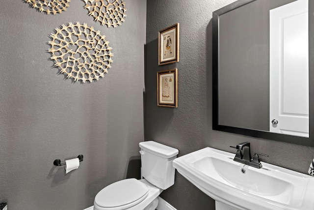 bathroom with a textured wall, a sink, and toilet