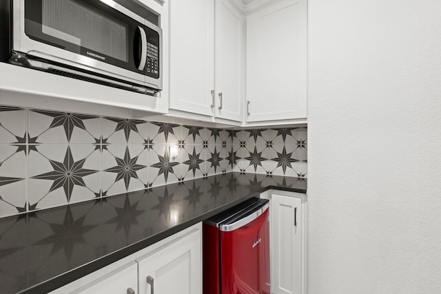 kitchen featuring dark countertops, stainless steel microwave, white cabinets, and decorative backsplash