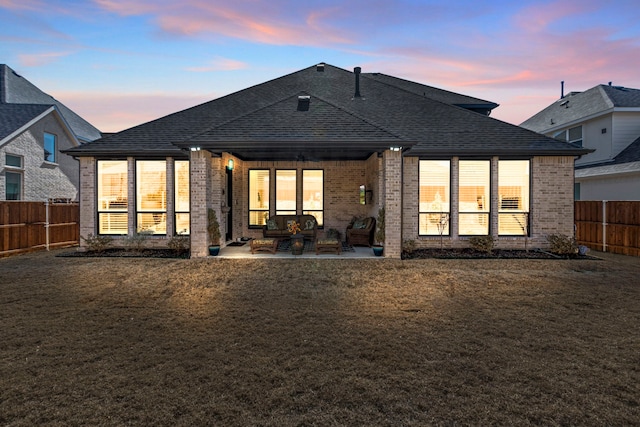 rear view of property with brick siding, a fenced backyard, roof with shingles, and a patio