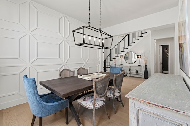 dining room featuring stairs, a decorative wall, a chandelier, and light wood-style floors