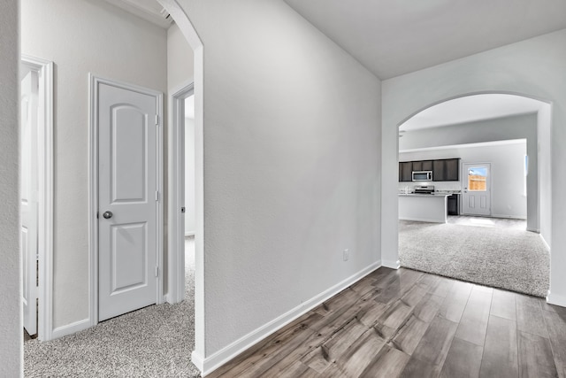 corridor with arched walkways, dark wood-style floors, and baseboards