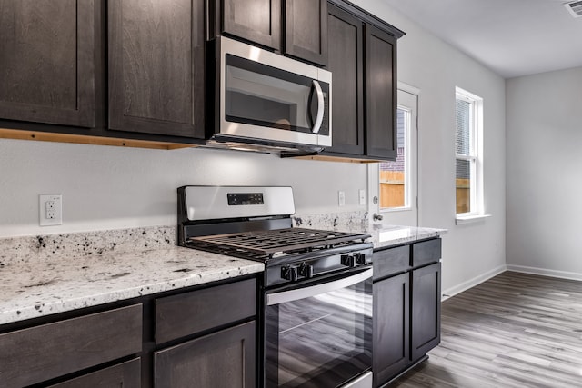 kitchen with dark brown cabinetry, baseboards, appliances with stainless steel finishes, light stone countertops, and light wood-style floors