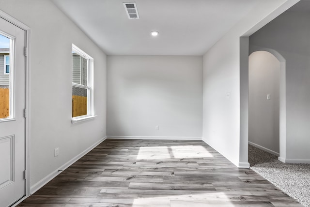 unfurnished room featuring light wood-type flooring, arched walkways, visible vents, and plenty of natural light