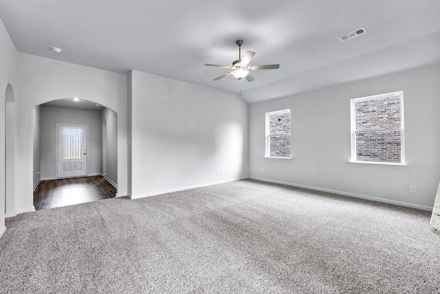 spare room featuring arched walkways, lofted ceiling, visible vents, dark carpet, and ceiling fan