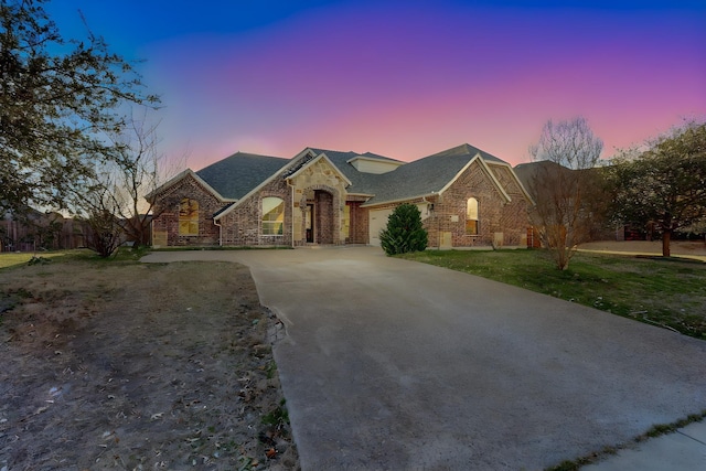 french country home featuring an attached garage, a front lawn, concrete driveway, and brick siding