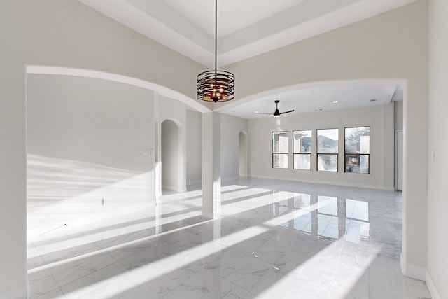 unfurnished room featuring arched walkways, baseboards, ceiling fan, marble finish floor, and a tray ceiling