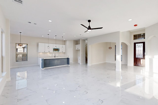 unfurnished living room with arched walkways, marble finish floor, visible vents, and a ceiling fan