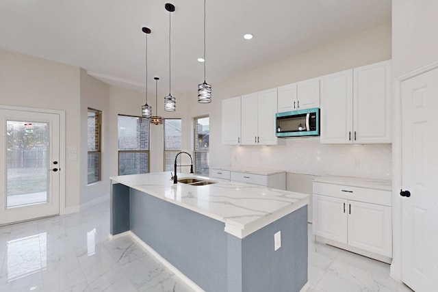 kitchen featuring marble finish floor, stainless steel microwave, a center island with sink, and a sink