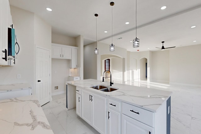 kitchen with marble finish floor, decorative light fixtures, a kitchen island with sink, a sink, and white cabinetry