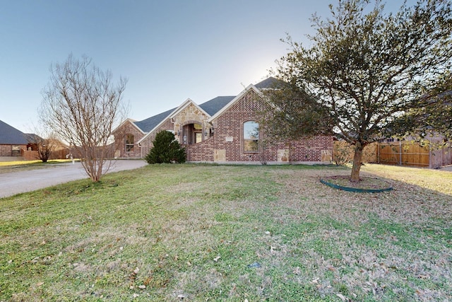 view of front of house with stone siding, brick siding, fence, and a front lawn