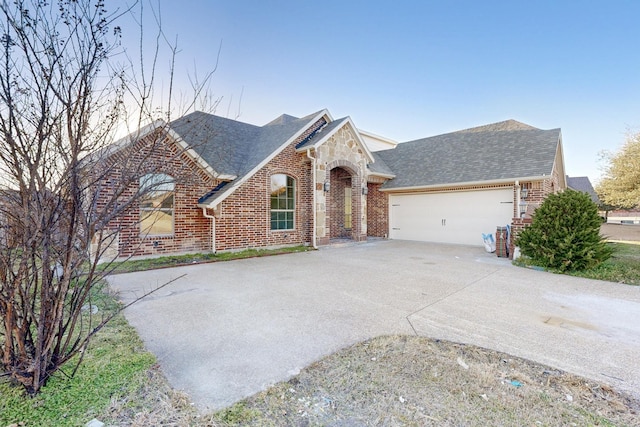 view of front of property featuring a garage, brick siding, driveway, and roof with shingles