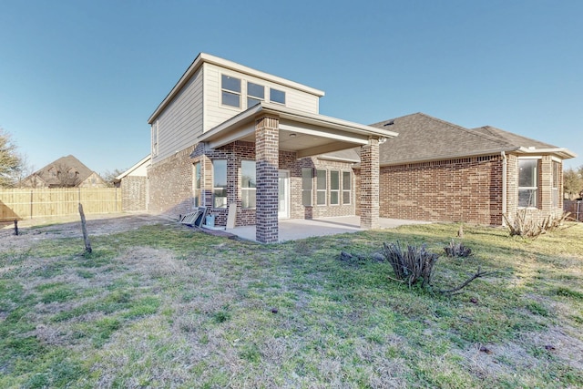 back of house featuring brick siding, fence, a patio, and a lawn