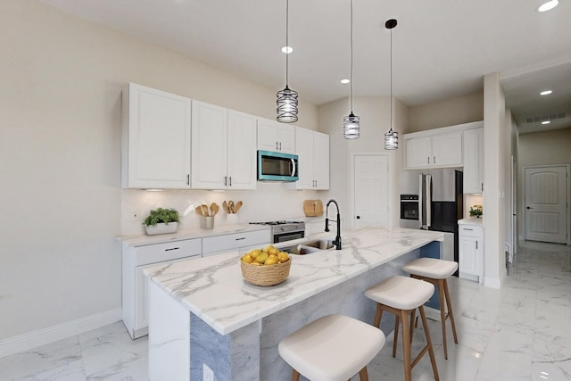 kitchen featuring stainless steel appliances, white cabinets, a sink, an island with sink, and light stone countertops