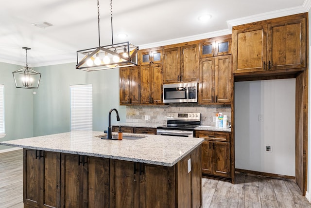 kitchen with appliances with stainless steel finishes, a kitchen island with sink, decorative light fixtures, and a sink