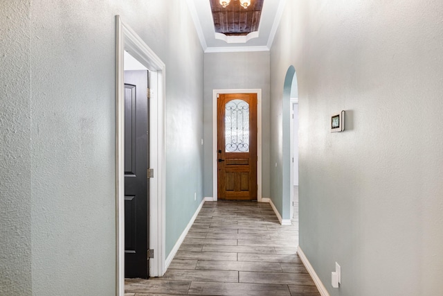 doorway to outside with baseboards, arched walkways, a textured wall, crown molding, and wood finish floors