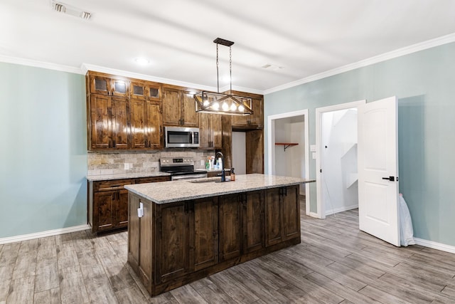 kitchen with light stone counters, stainless steel appliances, a sink, an island with sink, and decorative light fixtures