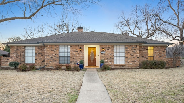 ranch-style house with a front yard, roof with shingles, a chimney, and brick siding