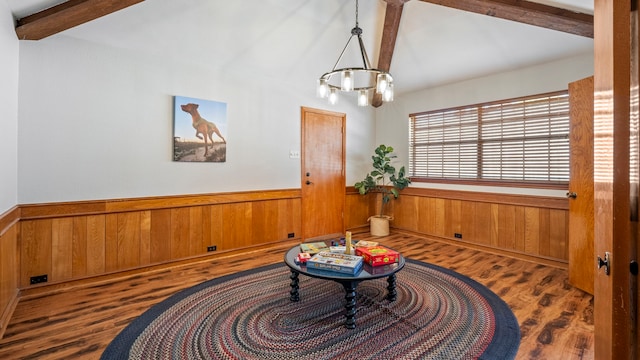 sitting room with lofted ceiling with beams, a notable chandelier, a wainscoted wall, wood walls, and dark wood-style floors