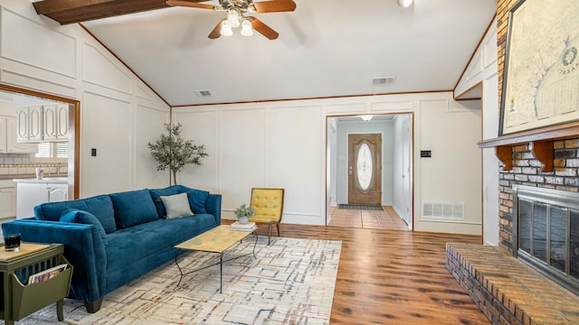 living area featuring vaulted ceiling with beams, visible vents, a decorative wall, and light wood-style flooring