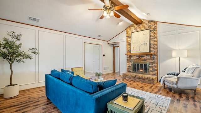 living room featuring a brick fireplace, visible vents, a decorative wall, and wood finished floors