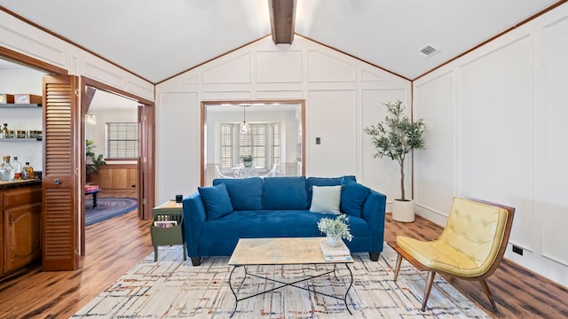 living room featuring vaulted ceiling with beams, light wood finished floors, visible vents, and a decorative wall