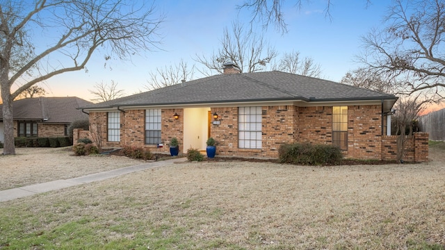 ranch-style home with brick siding, a chimney, a shingled roof, and a front yard