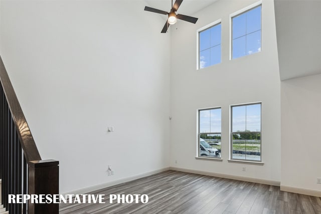 unfurnished living room with a ceiling fan, a towering ceiling, baseboards, and wood finished floors