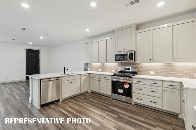 kitchen with stainless steel appliances, a peninsula, a sink, visible vents, and light countertops