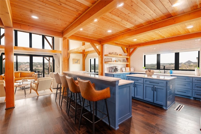 kitchen featuring a breakfast bar area, blue cabinetry, open shelves, light countertops, and dark wood-type flooring