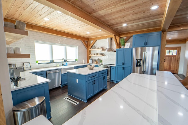 kitchen with blue cabinets, appliances with stainless steel finishes, wall chimney exhaust hood, open shelves, and beamed ceiling