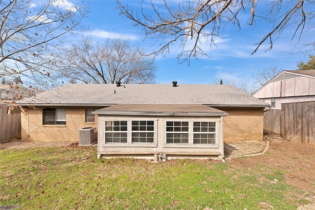 back of house featuring roof with shingles, fence, a yard, central air condition unit, and brick siding