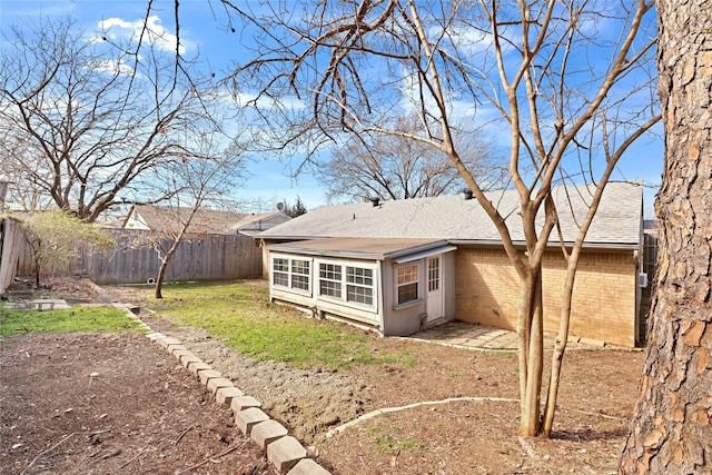 rear view of house featuring brick siding, roof with shingles, and a fenced backyard